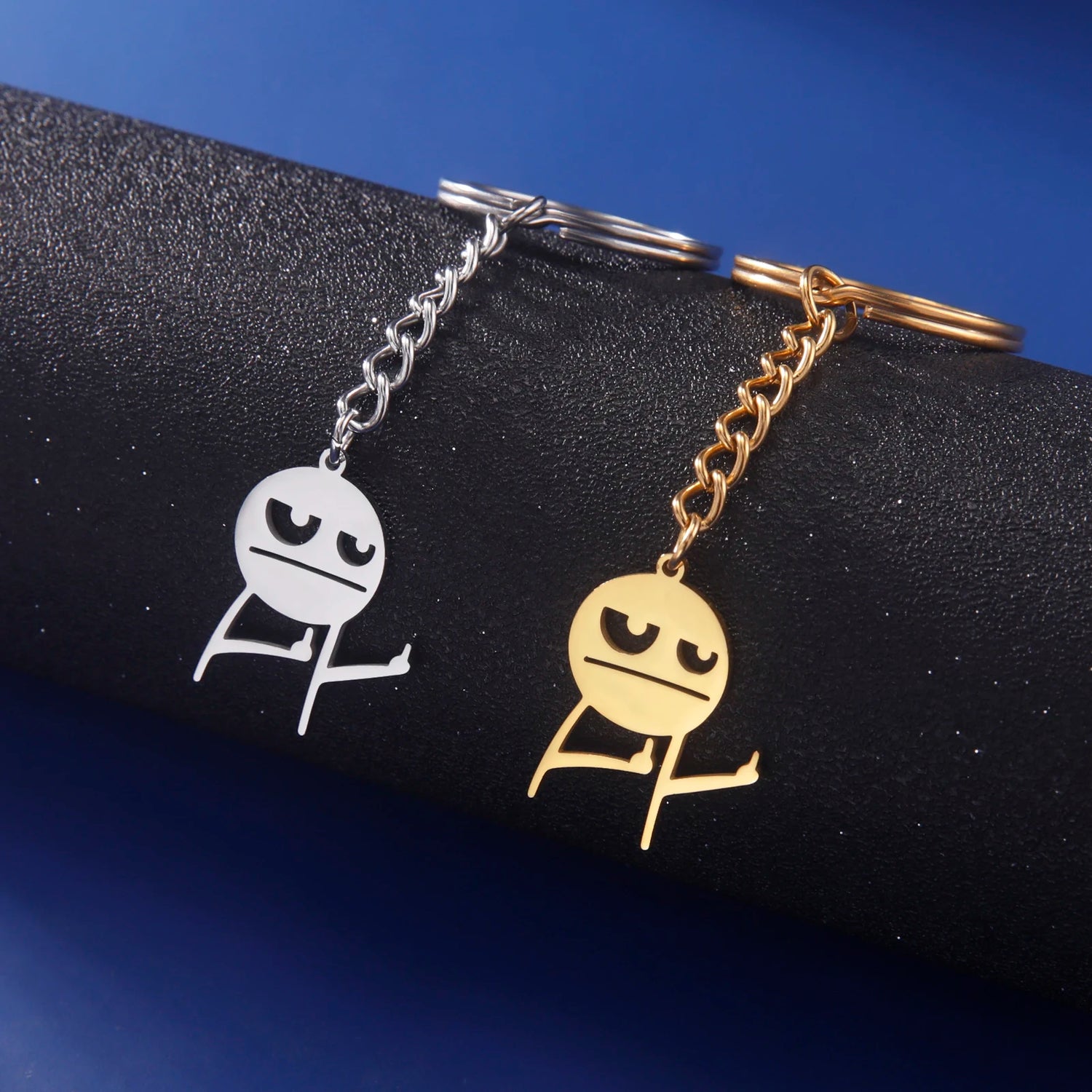 Gold and Silver Keychain holding up 2 middles fingers on a blue background resting on a black tube